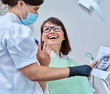Woman smiling with dentist while reviewing X-ray