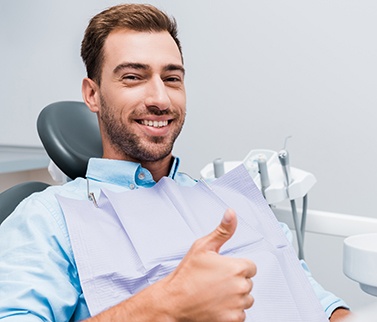 A happy bearded man smiling and giving a thumbs up in a dentist’s office
